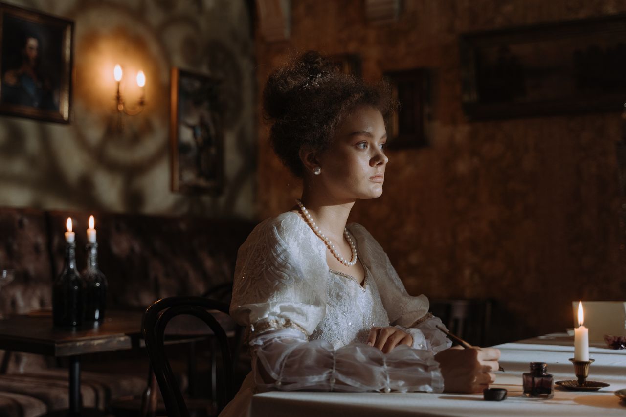 À propos A noblewoman in period attire writes by candlelight in an elegant, historic setting.